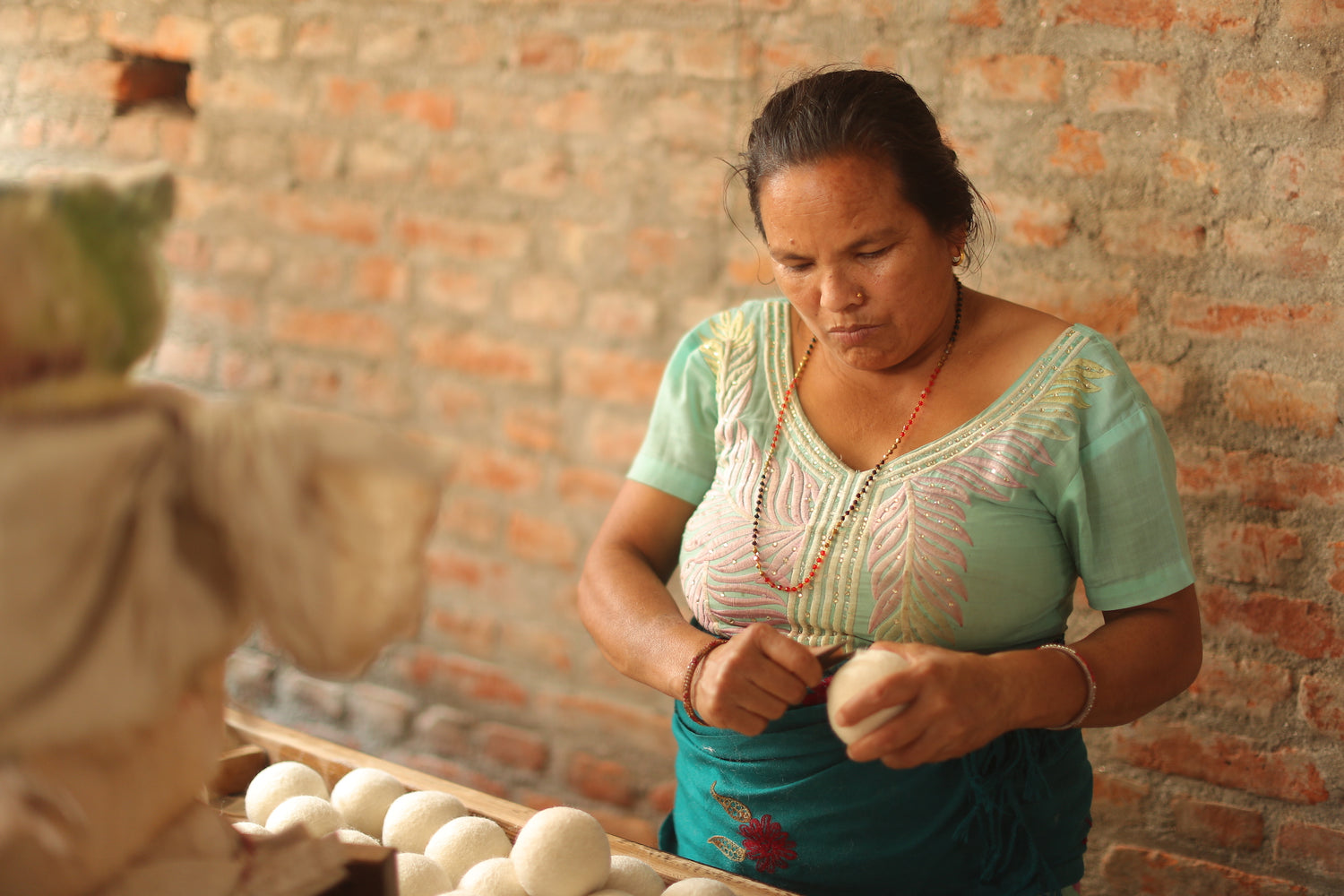 A woman is forming a wool ball. 