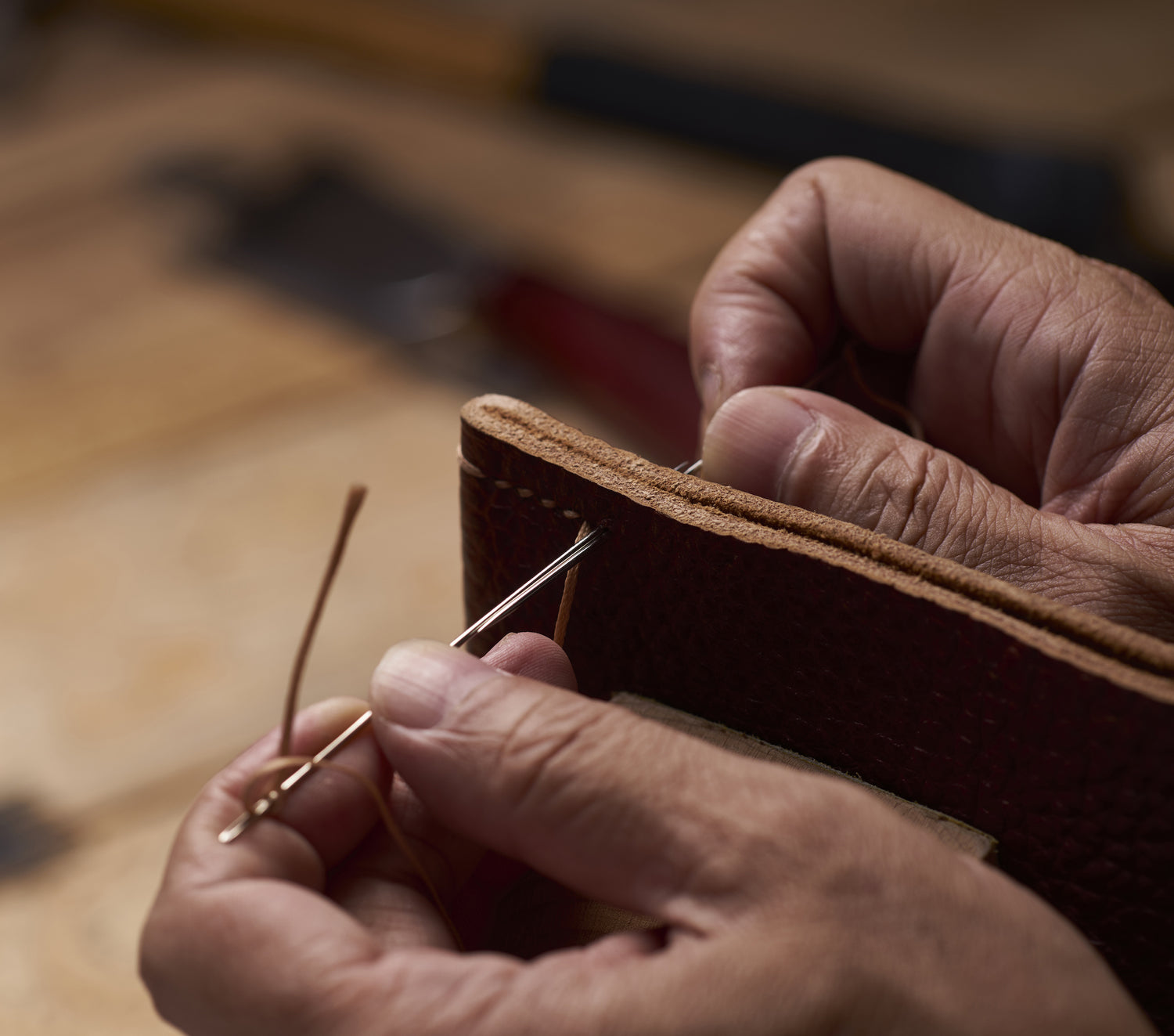 Two hands sewing together pieces of leather from Guatemala. 